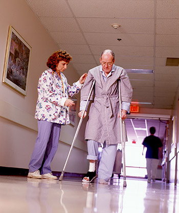 Nurse helps patient on crutches in hospital.